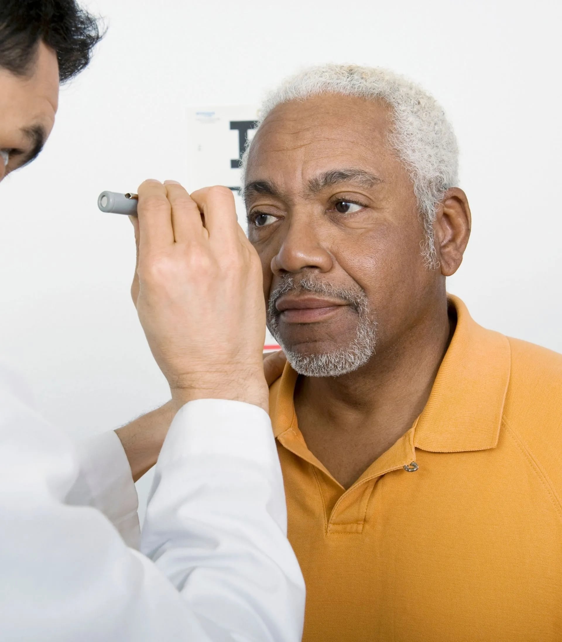 eye doctor shining light into older male patient’s eye performing eye exam