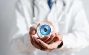 Doctor holds a model of a human eye with a bright blue iris in the palm of his hand as he explains corneal tattooing to a patient